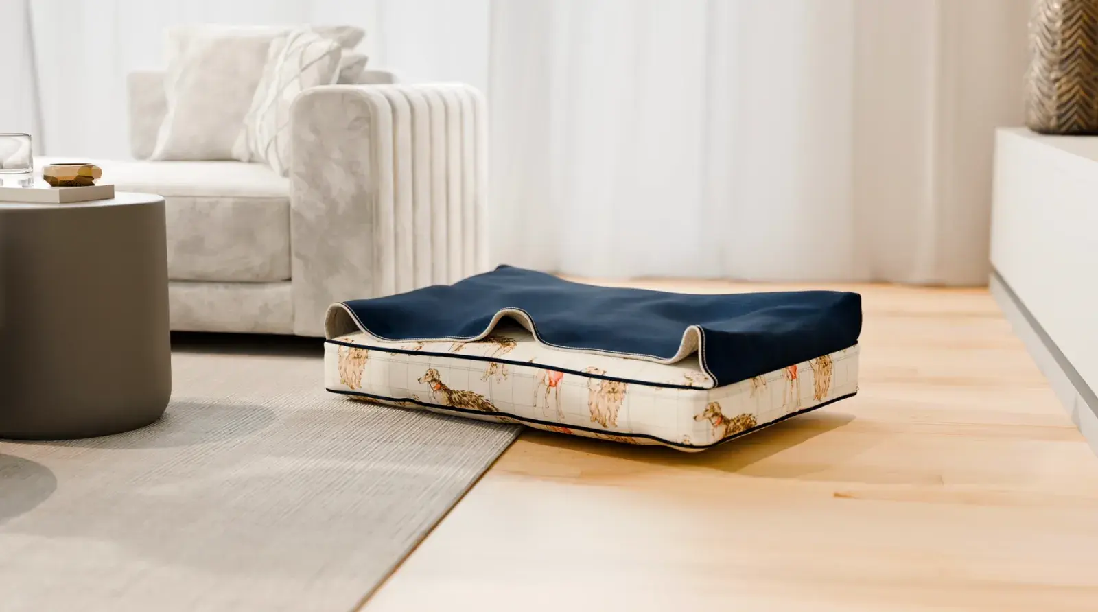 A Cave Dog Bed in a dog-print fabric with a navy hood on a light living room floor