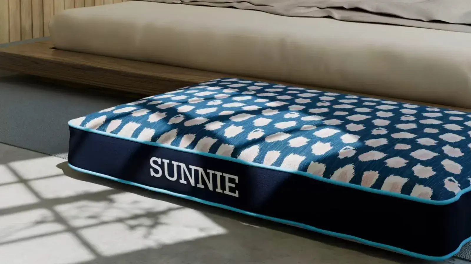 A Rectangle Dog Bed in navy with a blue dot top, embroidered Sunnie, beside a daybed